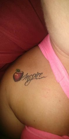 a woman with an apple tattoo on her upper arm and the word inspire written in cursive writing