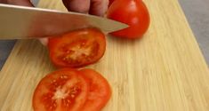 a person cutting tomatoes on a wooden cutting board