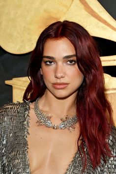 a woman with long red hair wearing a silver dress and statement necklace on her neck