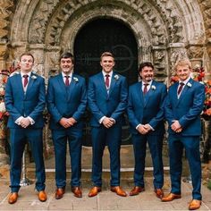 a group of men standing next to each other in front of a stone building wearing suits and ties