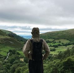 a man standing on top of a lush green hillside next to a lush green valley