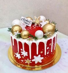 a red and gold christmas cake with white icing, ornaments and pine cones on top