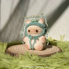 a small crocheted bear sitting on top of a piece of wood in the grass