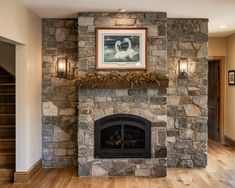 a stone fireplace in the middle of a room with wood flooring and framed pictures on the wall