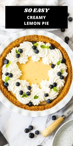 a lemon pie with whipped cream and blueberries in the middle on a white plate