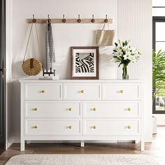 a white dresser sitting in a living room next to a plant and pictures on the wall