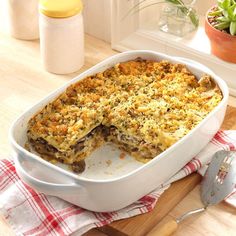 a casserole dish on a wooden table with a serving utensil next to it