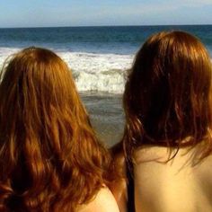 two women sitting on the beach looking out at the ocean