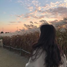 a woman standing in front of a field with tall grass and wind mills behind her