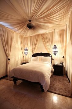 a bed sitting under a white canopy in a bedroom next to two lamps on either side of the bed