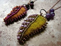 two necklaces with beads and bead work on them sitting on a stone surface