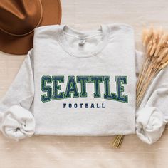 Get ready for game day with this cozy Seahawks football crewneck! Perfect for Seattle football tailgating, gifting, or showing off your football pride. 🎉 This unisex sweatshirt is the ultimate fan gift for him, her, or anyone who loves Seattle football. Hello there! 😊👋 If you're on the hunt for some seriously cozy sweatshirts, you've come to the right place! I'm absolutely passionate about what I do, and my mission is to make your shopping experience absolutely perfect. If you ever have any q Team Spirit T-shirt For Game Day In Winter, Game Day Fan Apparel Sweatshirt With Lettering, Winter Game Day T-shirt With School Spirit Style, School Spirit T-shirt For Game Day In Winter, Winter Game Day Varsity T-shirt, Varsity T-shirt For Game Day In Winter, Seahawks Game Day, Football Crewneck, Game Day Sweatshirt