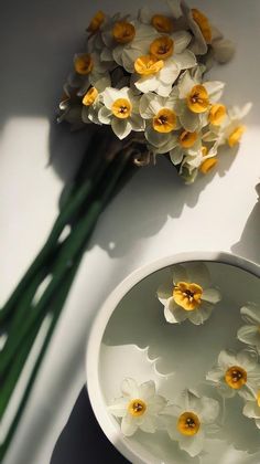 some flowers are sitting in a bowl next to the vase with it's reflection