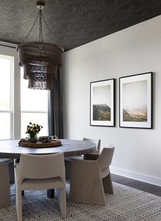 a dining room table with four chairs in front of two pictures hanging on the wall