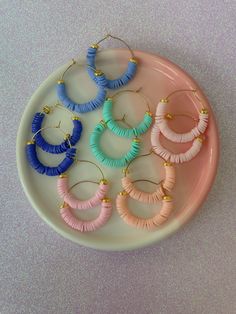 four pairs of hoop earrings on a plate with pink, blue and yellow beads hanging from them