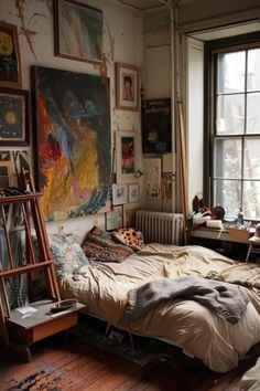 an unmade bed sitting next to a window in a room with lots of pictures on the wall