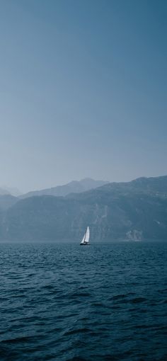 a sailboat sailing on the ocean with mountains in the background