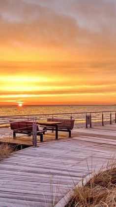 the sun is setting over the ocean and some benches are on the pier near the water