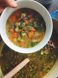 a person is holding a spoon over a bowl of soup