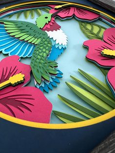 a paper cut bird sitting on top of a blue plate with pink and green flowers