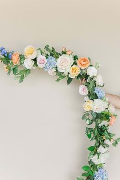 a woman is holding a floral arch with flowers on the top and bottom, in front of a white wall