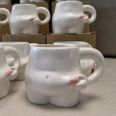 four white coffee mugs sitting on top of a table next to boxes with one cup in the shape of an elephant