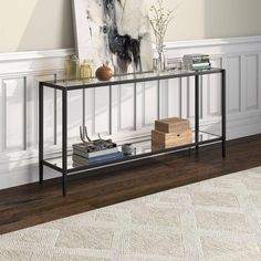 a black metal and glass console table in a living room with white walls, wood flooring and a painting on the wall