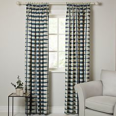 a white chair sitting in front of a window covered in blue and yellow curtains with an abstract pattern