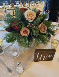 a centerpiece with flowers and greenery sits on a table at a wedding reception