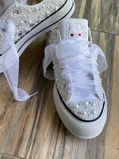 two pairs of white sneakers with bows and pearls on the soles, one is decorated with an i love you message