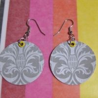 two pairs of earrings are sitting on a rainbow striped tablecloth, one is made from paper and the other is painted with an ornate pattern