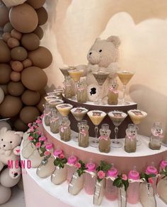 a teddy bear sitting on top of a table filled with drinks and desserts next to balloons