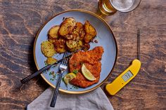 a plate with fried fish, potatoes and lemon wedges next to a glass of beer