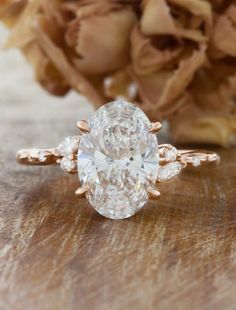 a close up of a diamond ring on a table with flowers in the back ground