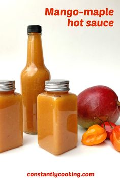 three jars filled with mango - maple hot sauce sitting next to some fruit and vegetables