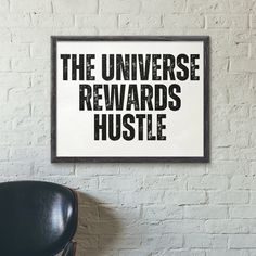 a black chair sitting in front of a white brick wall next to a sign that reads the universe reward hustle