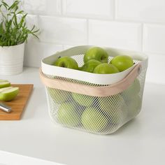 a basket filled with green apples sitting on top of a counter next to a cutting board