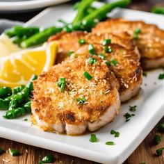 three scallops on a white plate with asparagus and lemon wedges