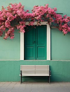 a white bench sitting in front of a green building with pink flowers growing over it