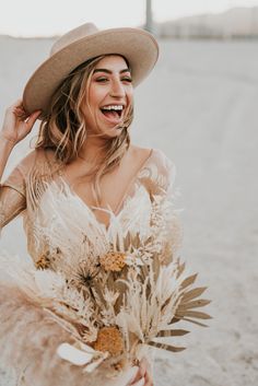 a woman wearing a hat and holding a bouquet in front of her face on the beach