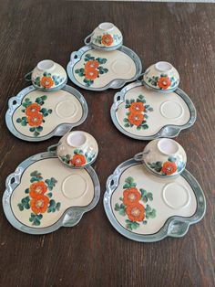 six orange flowers on white dishes sitting on a wooden table