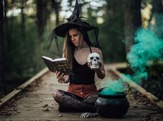 a woman in a witches costume sitting on a path reading a book and holding a skull