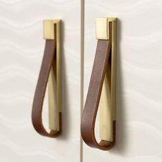 two brown handles on a white cabinet with leather straps hanging from it's sides