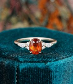 an orange and white diamond ring sitting on top of a blue velvet cushioned box