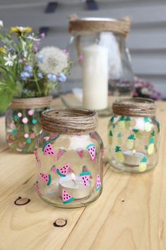 three mason jars with candles and flowers in them on a table next to a candle