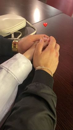 two people holding hands over a table with a white purse and red heart on it