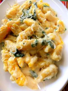 a white plate topped with pasta covered in cheese and spinach sauce on top of a colorful table cloth