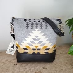 a gray and yellow bag sitting on top of a wooden table next to a potted plant