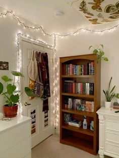 there is a book shelf in the room with many books on it and some plants