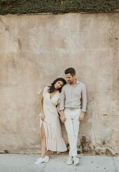 a man and woman standing next to each other near a wall with ivy growing on it